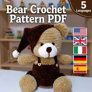 May include: A handmade crochet bear wearing a brown hat and dungarees. The bear has a white face and is seated. The image features the text "Bear Crochet Pattern PDF" and flags representing 5 languages.