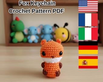 May include: An orange crochet fox keychain with a white chest and dark brown paws. The keychain is handmade and sits in front of a shelf with other crochet animals. Text on the image reads "Fox Keychain Crochet Pattern PDF".
