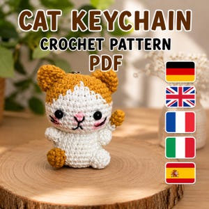 以下が含まれることがあります： かぎ針編みの猫のキーホルダーのPDFパターン。白とオレンジの毛糸で作られた小さな手作りの猫で、黒い目、ピンクの鼻、刺繍されたひげが特徴です。上部にはCAT KEYCHAIN CROCHET PATTERN PDFというテキストと5つの国旗が表示されています。