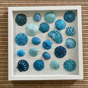 以下が含まれることがあります： 青とターコイズ色の貝殻のコレクションが白いフレームに収められています。貝殻は白い背景に配置されています。貝殻はサイズと形が異なり、複雑な模様のものもあります。
