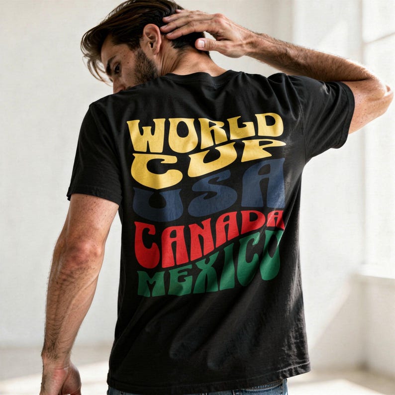 May include: Black t-shirt with the words "WORLD CUP USA CANADA MEXICO" in yellow, blue, red, and green, respectively. The text has a retro, wavy design. The shirt is a casual wear item.