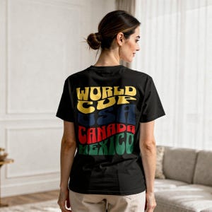 May include: Black t-shirt with the words "WORLD CUP USA CANADA MEXICO" in yellow, blue, red, and green. The shirt is worn by a person with their back to the camera.