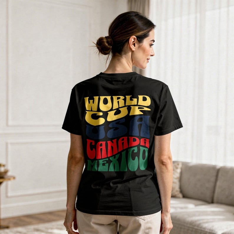 May include: Black t-shirt with the words "WORLD CUP USA CANADA MEXICO" in yellow, blue, red, and green. The shirt is worn by a person with their back to the camera.