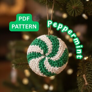 Può includere: Un ornamento natalizio a tema menta piperita all'uncinetto con strisce verdi e bianche. L'ornamento è appeso a uno spago naturale sullo sfondo di un albero di Natale. Il testo sull'immagine recita "PDF PATTERN" e "Peppermint".