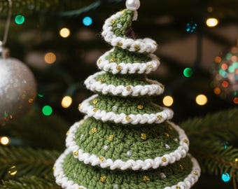 May include: A handmade, green crochet Christmas tree ornament with white trim and gold accents. The tree is tiered, with a spiral top and a white string for hanging. The ornament is displayed on a Christmas tree.