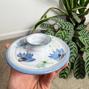 May include: A ceramic serving dish with a central dip bowl and a surrounding plate. The plate is white with blue floral designs and a light blue rim. The dip bowl is white with a dark rim.