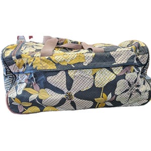 May include: A floral patterned travel bag with a navy blue background, large yellow and white flowers, and tan handles. The bag has a zipper closure and a striped pattern on the side.