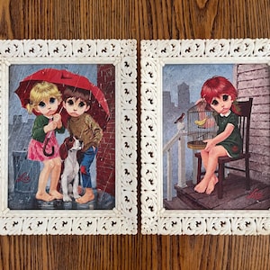 May include: Two framed prints featuring Big Eyes art. One shows two children under a red umbrella with a dog in the rain. The other depicts a girl with a birdcage. Both are in ornate white frames.