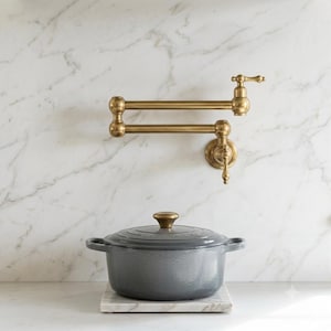 Peut inclure: Un robinet remplisseur de casserole mural en laiton avec un bras articulé double et une poignée à levier, placé au-dessus d'une cocotte ronde en fonte émaillée grise avec couvercle et poignées latérales, posée sur une base carrée en marbre.