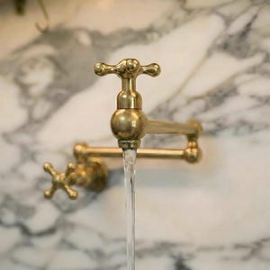 Peut inclure: Un robinet remplisseur de casseroles mural en laiton avec un bras articulé à double joint et une poignée en croix. Le luminaire métallique présente une finition polie et un jet d'eau vertical et régulier s'écoule du bec.