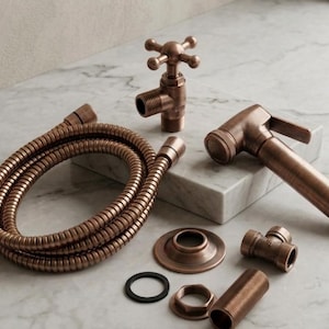 Può includere: Un set per bidet color rame composto da un tubo flessibile in metallo, una valvola con manopola a croce, un erogatore a mano, una rosetta circolare, un raccordo a T, un'estensione filettata e una guarnizione in gomma nera.