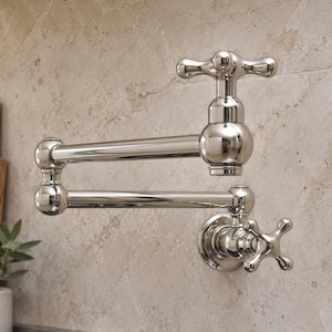 May include: A polished chrome wall-mounted pot filler tap featuring a double-jointed articulating arm and two cross-style handles. The fixture has a reflective metallic finish with a central spout and a circular base plate attached to the wall.
