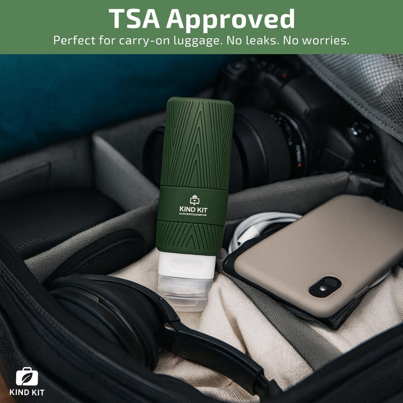 May include: A green travel bottle with a white dispenser, inside a black carry-on bag. The bottle has a textured design and the text "KIND KIT". The text "TSA Approved" is at the top.