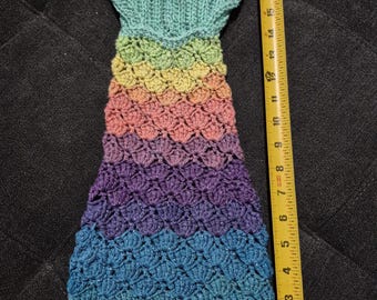 Op de afbeelding: Een handgemaakte, gehaakte zeemeerminstaart in tinten blauw, paars, roze, geel en groen. De staart is ongeveer 48 cm lang, met een geschulpte patroon en een vinachtig bovenstuk.