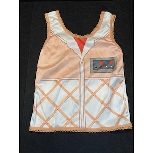 May include: A sleeveless tank top with a retro design. The top features a peach-colored front with a white diamond pattern and a small control panel graphic. The neckline and hem are trimmed with a scalloped edge.