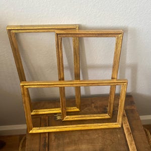 Pode incluir: Três molduras douradas de tamanhos diferentes, empilhadas umas sobre as outras. As molduras são de madeira e têm um design simples e clássico.