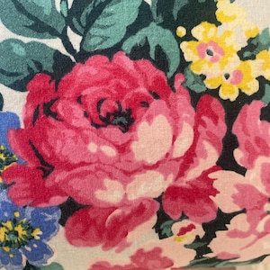 Puede incluir: Primer plano de un estampado floral con grandes rosas rojas y rosas, flores azules y amarillas y hojas verdes sobre un fondo blanco. El diseño es detallado y parece estar impreso en tela, mostrando un tema botánico clásico.