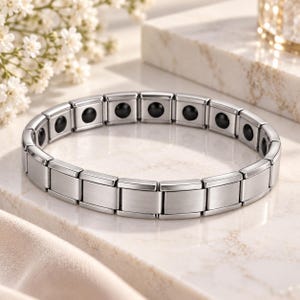 Peut inclure: Un bracelet à maillons argentés composé d'une série de segments métalliques rectangulaires. Chaque segment contient une petite incrustation circulaire noire. Le bracelet présente une conception modulaire avec une finition métallique polie.