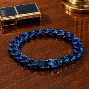 May include: A vibrant blue metallic curb chain bracelet featuring interlocking polished links and a secure integrated clasp mechanism. The bracelet has a high-gloss finish that reflects light across its curved surfaces, creating a bold and uniform appearance.