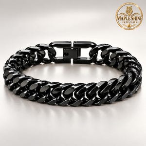 Peut inclure: Un bracelet gourmette noir poli composé de maillons métalliques épais et entrelacés avec un fermoir rectangulaire sécurisé. Le logo doré circulaire avec une chouette et le texte MAPLESHINE JEWELRY est visible en haut.