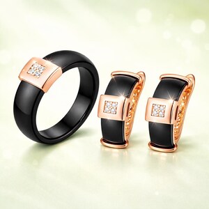 May include: A jewelry set consisting of a black ceramic ring and a pair of matching hoop earrings. Each piece features a rose gold-toned square accent set with four small clear stones, creating a cohesive look with polished surfaces.