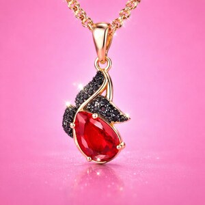 May include: A gold-toned pendant necklace featuring a large, pear-shaped red gemstone as the centrepiece. The pendant is accented with small, dark black stones arranged in a curved, wing-like pattern above the red stone, suspended on a gold chain.