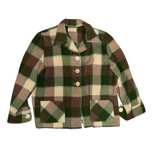 Puede incluir: Una chaqueta de manga larga con un patrón de cuadros grandes en tonos verde bosque, marrón y crema. La chaqueta incluye un cuello puntiagudo, un cierre frontal con cuatro botones claros, dos bolsillos cuadrados delanteros y puños abotonados.