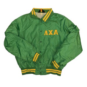 May include: A green nylon bomber jacket featuring a snap-button front closure, a fold-down collar, and ribbed cuffs and hem with yellow stripes. The Greek letters AXA are embroidered in yellow on the upper right chest area of the garment.