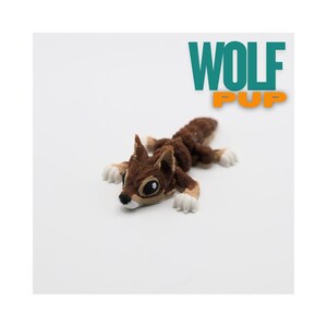 May include: A brown and white wolf pup figurine lying on a white surface. The figurine has large eyes and a detailed fur texture. The text "WOLF PUP" is displayed in teal and orange.