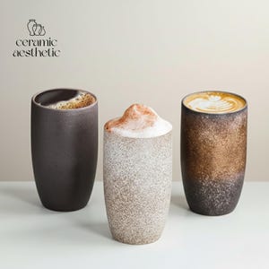 以下が含まれることがあります： さまざまなコーヒーが入った3つのセラミックコーヒーマグ。マグカップは円筒形で、テクスチャード加工が施されています。1つはコーヒーが入った濃い茶色、もう1つは泡状のトッピングが付いたベージュ、3つ目はラテアートが入った茶色です。「ceramic aesthetic」の文字が左上にあります。
