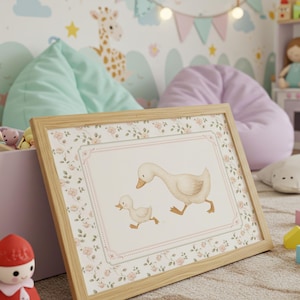 Pode incluir: Uma impress&atilde;o emoldurada com uma ilustra&ccedil;&atilde;o em aquarela de um ganso e um ganso. A obra de arte tem uma borda floral e uma moldura de madeira clara. A imagem est&aacute; em um quarto infantil com brinquedos e itens decorativos.
