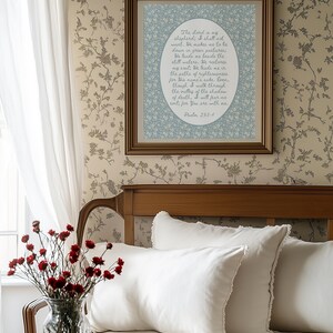May include: A framed print with a floral design and text from Psalm 23:1-4 hangs on a wall with a floral pattern. The room features a bed with white pillows and a vase of red flowers.