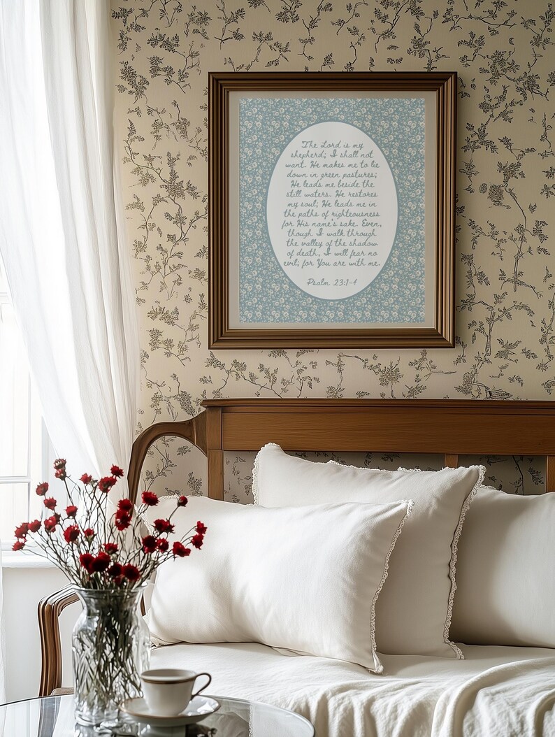 May include: A framed print with a floral design and text from Psalm 23:1-4 hangs on a wall with a floral pattern. The room features a bed with white pillows and a vase of red flowers.