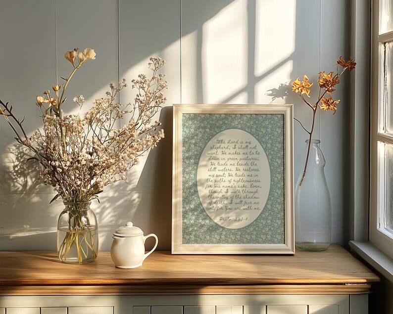 May include: A framed print with a floral background and text, a white teapot, and a clear glass vase with dried flowers sit on a wooden surface. A second vase with dried flowers is next to a window.