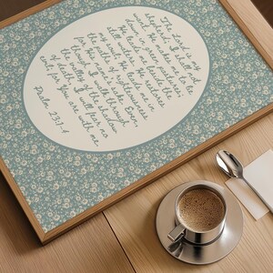 May include: Wooden framed print with a floral patterned background and an oval-shaped text area. The text is a religious quote from Psalm 23:1-4. A cup of coffee and a spoon are on the wooden surface.