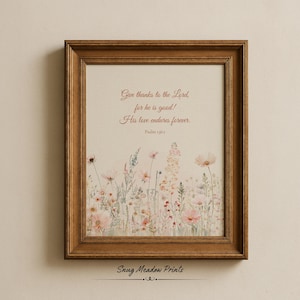 May include: A framed print with a wooden frame. The print features a floral illustration in soft pinks and greens, with the text "Give thanks to the Lord, for he is good! His love endures forever. Psalm 136:1." The bottom of the print reads "Snug Meadow Prints."