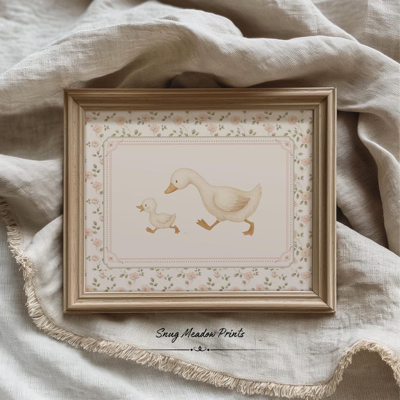 Pode incluir: Uma impress&atilde;o emoldurada com uma ilustra&ccedil;&atilde;o em aquarela de uma m&atilde;e pata e seu patinho. A obra de arte est&aacute; definida dentro de uma borda floral e uma moldura de madeira clara. O texto "Snug Meadow Prints" est&aacute; na parte inferior.