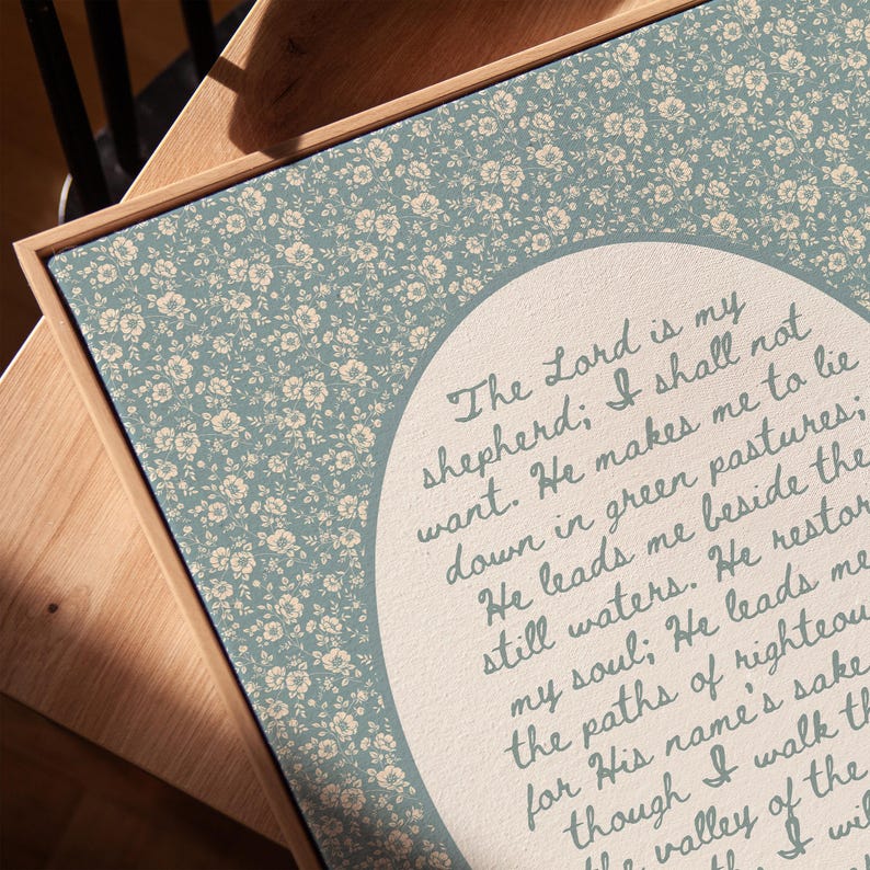May include: A framed canvas print with a light blue floral pattern background and a central oval containing script. The script reads, "The Lord is my shepherd; I shall not want."