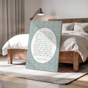 May include: A canvas print featuring a floral pattern in shades of blue and white. The print displays an oval-shaped text box with a religious quote from Psalm 23:1-4 in a handwritten style font. The canvas is displayed on a wooden bed frame.