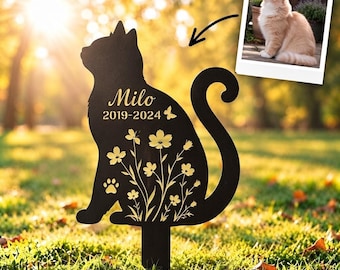 May include: A black metal cat-shaped garden stake featuring a cutout floral design, a paw print, and the engraved text "Milo 2019-2024". A small inset photograph shows a ginger cat, with an arrow pointing from the photo to the stake.