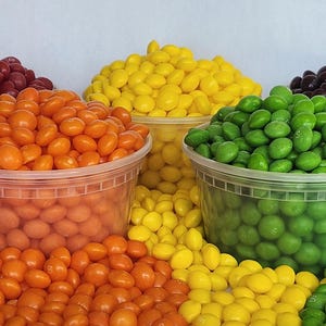 May include: An assortment of colorful candies in clear plastic containers. The candies are in shades of red, orange, yellow, green, and brown. Some candies are spilling out of the containers. The candies appear to be a hard shell type.