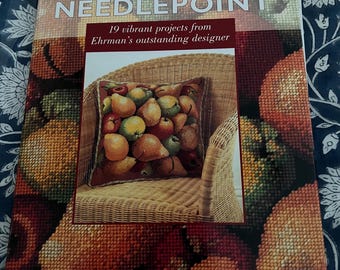 May include: A softcover book titled Elian McCready's NEEDLEPOINT: 19 vibrant projects from Ehrman's outstanding designer. The cover features a needlepoint pillow depicting a collection of pears resting on a wicker chair against a fruit background.