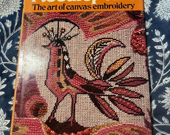 May include: A softcover book titled Needlepoint: The art of canvas embroidery by Mary Rhodes. The cover features a needlepoint illustration of a stylized bird in shades of pink, red, and orange against a textured background of canvas stitches.