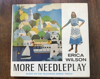 May include: A hardcover book titled More Needleplay by Erica Wilson, based on the television series Erica. The cover features a needlepoint illustration of a coastal village with a lighthouse and a photograph of a person wearing a blue and white outfit.