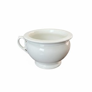May include: A white, ceramic chamber pot with a rounded body, a small handle, and a wide rim. The pot sits on a small, circular base. The glossy finish reflects light, highlighting its smooth surface.