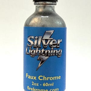 Può includere: Una bottiglia di vetro trasparente con tappo nero, riempita con un liquido argentato. L'etichetta blu riporta le scritte "Silver Lightning" e "Faux Chrome". Contenuto: 60 ml. È visibile il sito web firekrome.com.