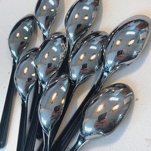 Op de afbeelding: Een verzameling glanzende chromen lepels met zwarte handvatten. De lepels zijn in een cluster gerangschikt en reflecteren licht. De tekst "FIRE KROME" wordt in een witte rechthoek rechtsonder weergegeven.