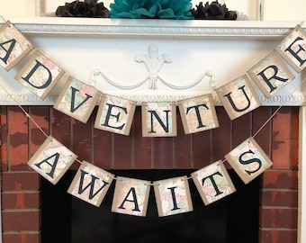 May include: A brown and white map-themed banner with the text "Adventure Awaits" in black letters. The banner is strung across a white fireplace mantel.