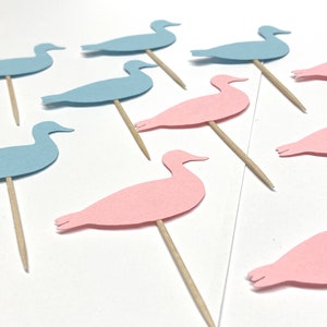 May include: A set of blue and pink paper duck cake toppers. The ducks are cut out of paper and attached to wooden skewers.