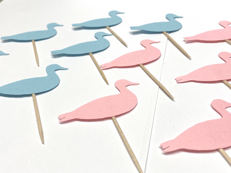 May include: A set of blue and pink paper duck cake toppers. The ducks are cut out of paper and attached to wooden skewers.